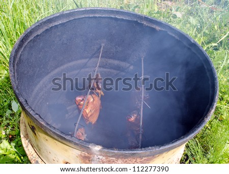 Ecologic fish smoke in smokehouse made of old rusty barrel.