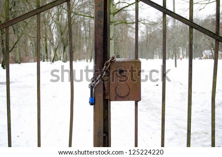 closeup of chain and lock closed retro rusty steel park gates in winter.