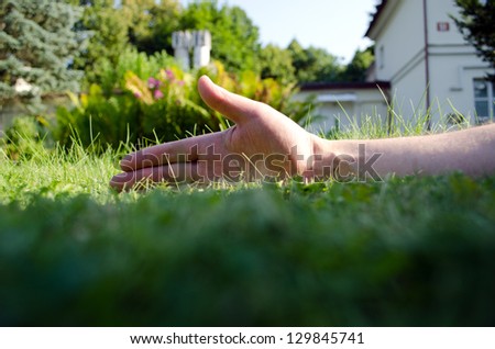 Human hand on garden meadow lawn grass and retro building fragment in background.