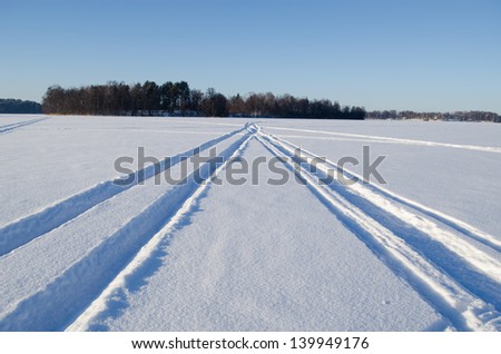 Snowmobile winter transport wheel marks left on frozen lake snow.