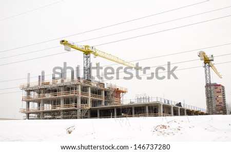 high building under construction and cranes on background of cloudy sky and winter snow.