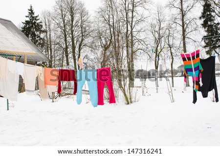 colorful washed wet clothes loundry dry hang on rope in house yard in winter.