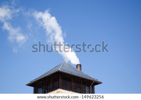 modern tin covered roof and white smoke rise from round chimney pipe on background of dark blue sky.