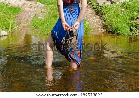 female legs with blue dress standing wade into the fast flowing stream summer nature park