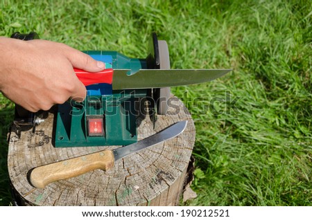 Hand grinder knife with electric tool on outdoor log.