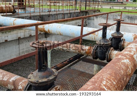 Rusty big tap valve gate and pipes in water treatment plant and dirty liquid bubble in background.