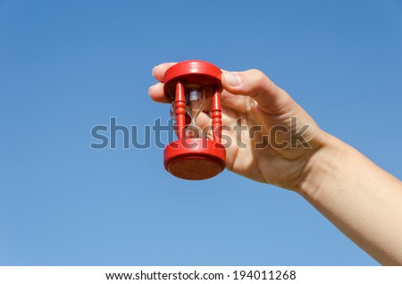 red wooden old hourglass in female hand on blue sky background
