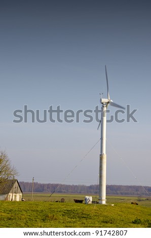 Windmill in the countryside. Farm building and the cows grazing around.