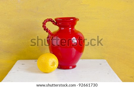 Still life. Red vase and yellow lemon on a shelf.