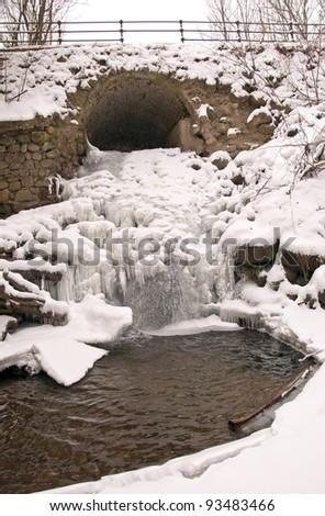 Stream water flow through arch waterfall ice icycle frozen in winter.