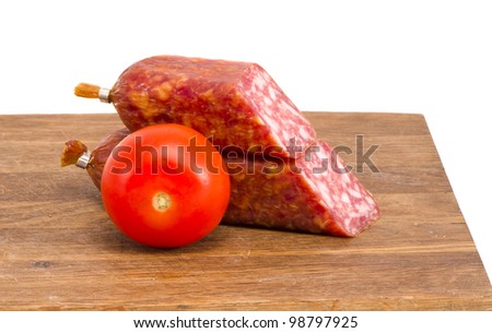 cut smoked sausage pieces and tomato on cutting board isolated on white background.
