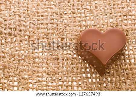 greeting card for Valentine\'s Day with chocolate heart symbol with needle on fabric sack texture background