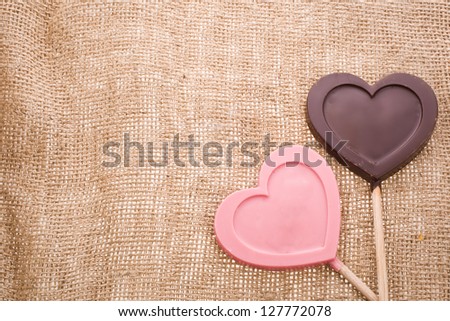 greeting card for Valentine\'s Day with chocolate hearts symbol lollipops  with needle on fabric sack texture background