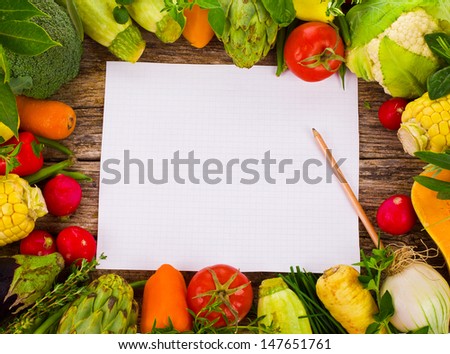 Topic cooking - lots of different vegetables and herbs on an old woodenand paper notebook for recipes board as a background