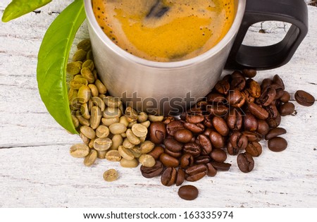 two types of coffee beans and brew coffee in a steel mug decorated with fresh leaves