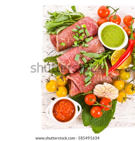 meat, a large piece of fresh meat, beef, to be on the old white boards, decorated with greens and vegetables and bowls with sauces  isolated on white background