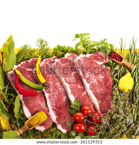 fresh meat - fresh steaks on a yellow mat, fresh herbs and vegetables \
isolated on white background
