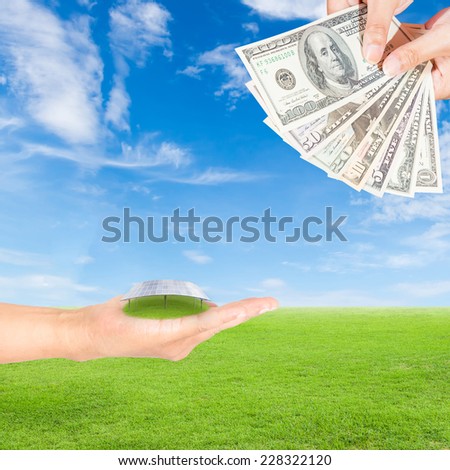 Carbon credits concept,hand holding solar panels and US Dollars banknote against green field and blue sky background