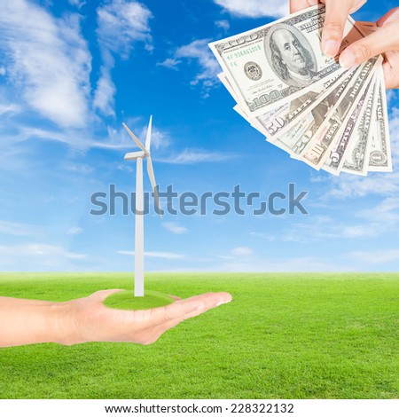 Carbon credits concept,hand holding wind turbine and US Dollars banknote against green field and blue sky background