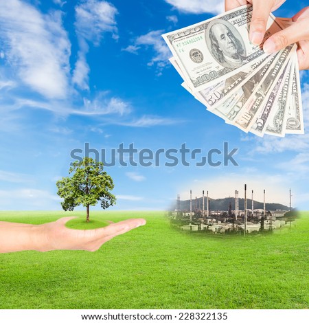 Carbon credits concept,hand holding tree and US Dollars banknote with oil refinery plant against green field and blue sky background