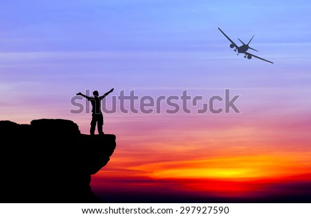 Silhouette of a man on the rock and silhouette commercial plane flying at sunset