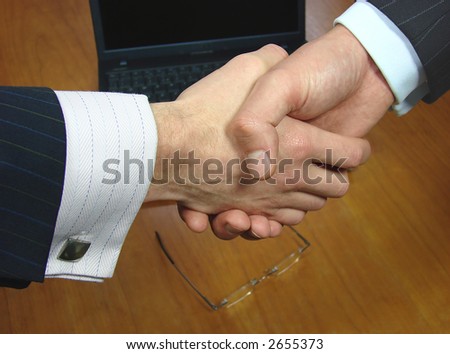 Focus on handshake over a desk with glasses and laptop in the background