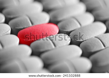 Red pill in row of monochrome pills. Macro image.