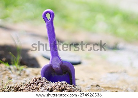 Violet baby shovel stuck in the sandbox. Macro image.