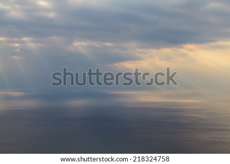 Beams of the sun make the way through clouds and fall on the sea.