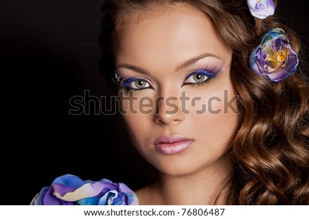 Pretty brunette young woman with creative makeup and flower in curly hair on white background