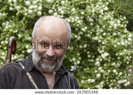 Smiling bald man with a beard against the backdrop of bush Spiraea betulifolia