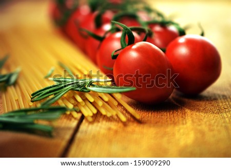 Essential Italian Food Ingredients. Shallow Depth Of Field Image Of Vine Tomatoes, Rosemary Herb And Dried Pasta. Selective Warm Lighting. Copy Space.