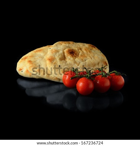 Stacked, warm Indian naan breads with dew covered tomatoes against a black background with soft reflections. Copy space