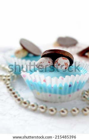 Iced cupcakes with mini chocolate eggs and dark chocolate discs against a white background. Shallow depth of field. Copy space.