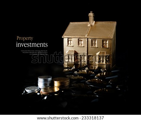 Concept image for property investment. Creatively lit gold house and stacked coins against a black background. Copy space.