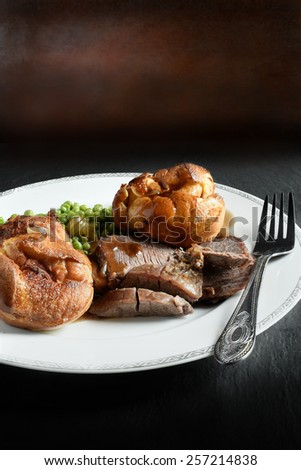 A curated image of topside roast beef, roast potatoes and traditional Yorkshire pudding in a restaurant setting against a dark background with copy space. Concept image for a Sunday lunch menu design.