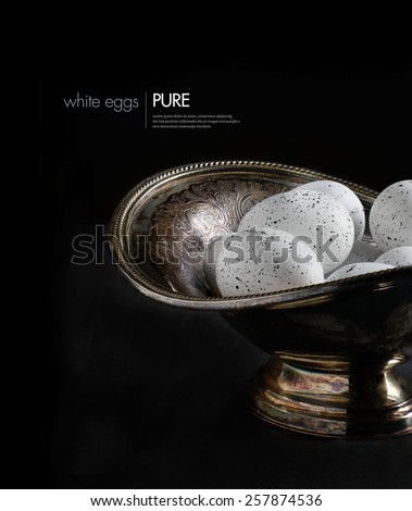 Creative and stylishly lit white speckled eggs in a beautiful antique Victorian scalloped bowl against a dark background. Concept image for Easter, pension funding, financial investments. Copy space.