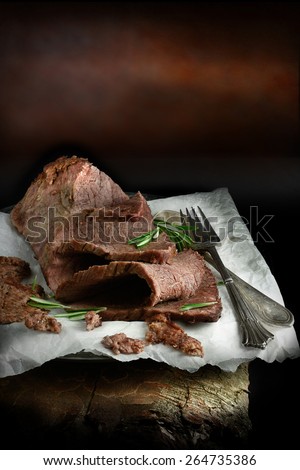 A curated image of perfectly cooked prime topside roast beef, sliced and ready to eat against a dark, rustic background with copy space. Concept image for a restaurant Sunday lunch menu cover design.