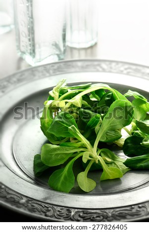 Summer styled, brightly lit image of a fresh Lamb lettuce salad on an antique pewter plate against a light background. Copy space.