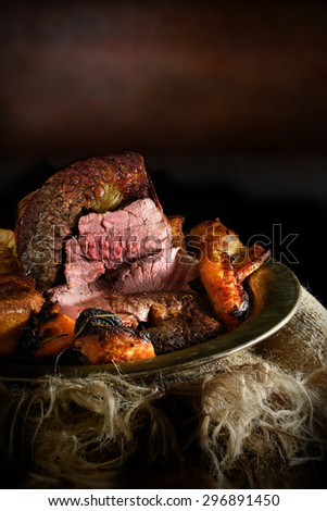 Creatively lit beef brisket in a rustic setting with roasted root vegetables of butter squash, carrot and onions. Sunday lunch concept image, perfect for your restaurant menu cover design. Copy space.