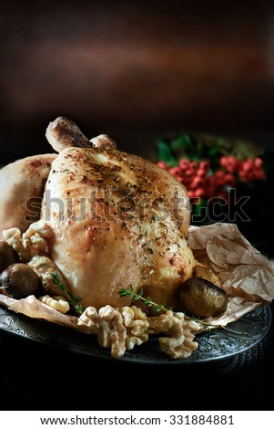 Creatively lit traditional Christmas whole roast chicken with mushrooms and walnuts, seasoned with thyme herbs against a festive, rustic background with generous accommodation for copy space.