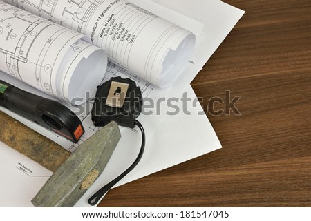 Construction drawings, tape measure, hammer and building level on a wooden surface. Desk builder