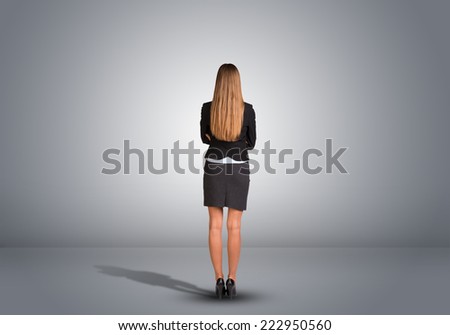 Businesswoman in suit standing in an empty gray room. Rear view. Hands crossed on his chest