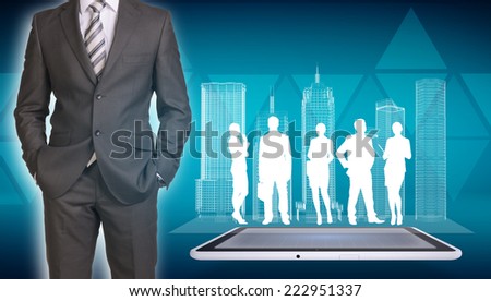 Businessman in suit standing and holds hands in pockets. Glowing wire-frame buildings and business silhouettes on screen tablet pc as backdrop