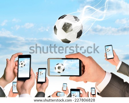 Hands holding smart phones and shoot video as falling soccer ball. Sky with clouds on background