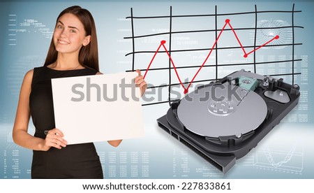Smiling beautiful businesswoman in dress hold empty paper sheet. Open HDD are located near. Graph as backdrop