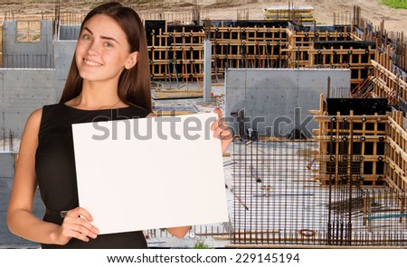Beautiful woman smiling and hold empty paper sheet. Construction site as backdrop. Industrial concept