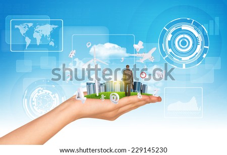 Hand holds city of skyscrapers on green grass and businessman walking forward. Fying letters near hand. Sky with clouds as backdrop