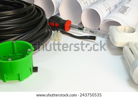 Drawing rolls, triple cable, screwdrivers, test pen, terminal block, wall socket, socket box, lamp on white surface