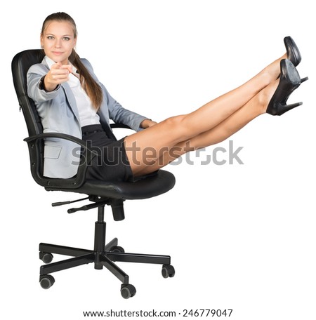 Businesswoman sitting on office chair with her feet up on anything, pointing finger at camera. Isolated over white background